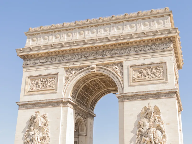 The Arc de Triomphe shot from below, its sculpted reliefs standing out against a blue sky